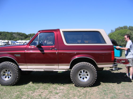 Side view of a red 1996 Ford Bronco with a tan top. Man loading a blue bin into the back