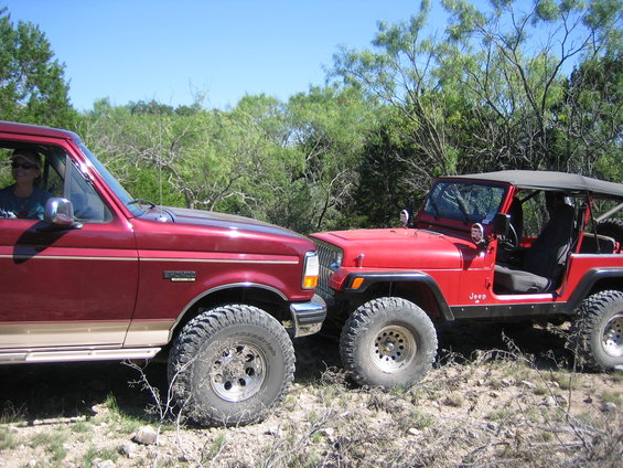 Red 1996 Ford Bronco parked next to a red Jeep Wrangler on a dirt road