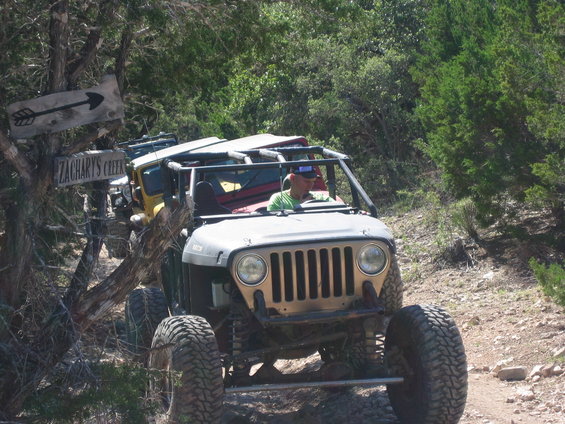 Several off-road Jeeps driving on a dirt trail next to a wooden sign pointing to Zachary's Creek
