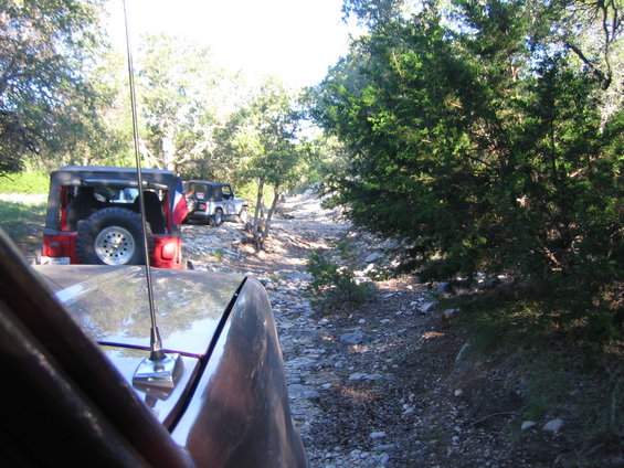 Red Jeep Wrangler rear view, spare tire mounted, Texas flag on antenna, driving on rocky trail