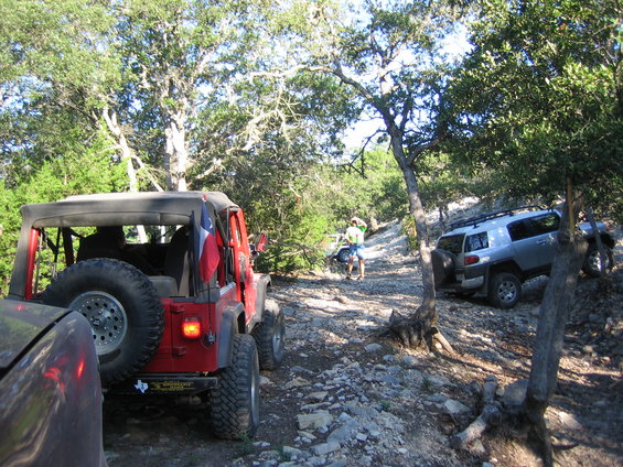 Red Jeep Wrangler rear view with Texas flag, silver Toyota FJ Cruiser on rocky trail