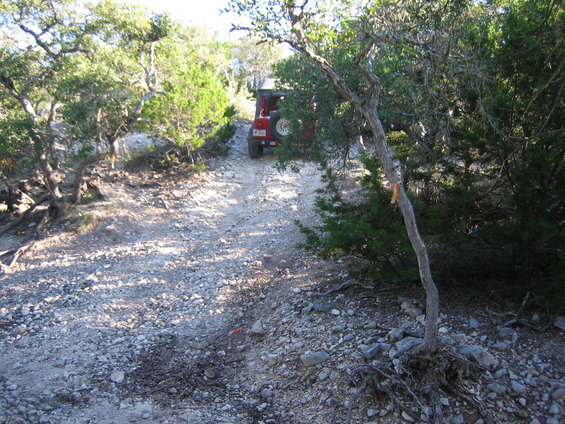 red Jeep Wrangler driving up a rocky, wooded trail