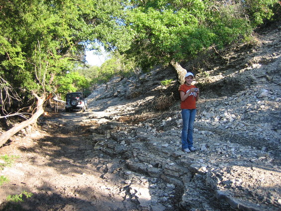 Silver Jeep Wrangler on a dirt road with a girl standing on a rocky incline