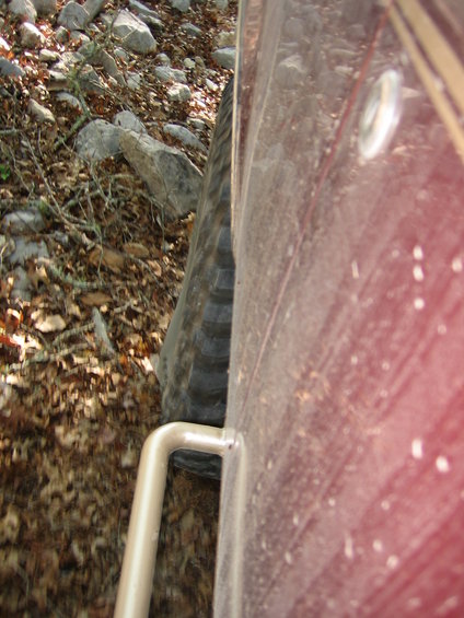 Close-up of a vehicle's tire and side panel on a rocky, leaf-strewn trail