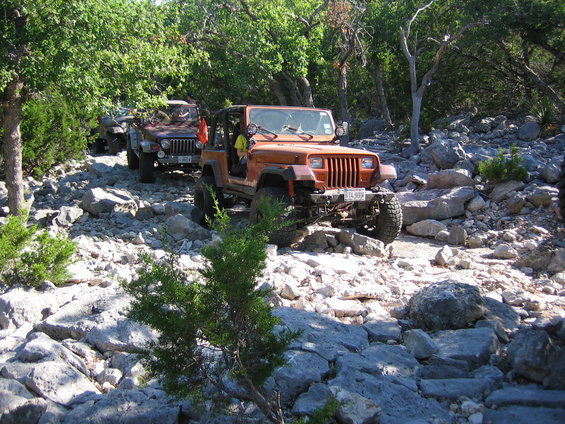 Orange Jeep Wrangler driving on a rocky trail with trees