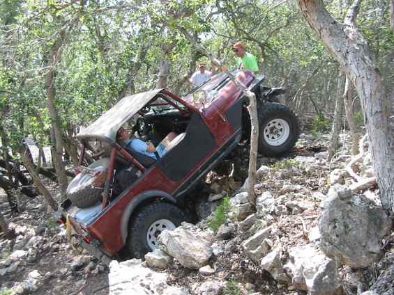 Red Jeep Wrangler tilted on a rocky trail with people watching