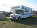 1996 Ford Bronco - A white motorhome with blue racing stripes is parked on a grassy field, accompanied by a tent and several other vehicles.