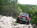 1996 Ford Bronco - A red Jeep Wrangler navigates a rocky off-road trail surrounded by trees.