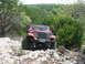 1996 Ford Bronco - A red Jeep Wrangler navigates a challenging rocky terrain on an off-road trail.