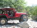 1996 Ford Bronco - A red Jeep Wrangler is shown driving over a large rock on a trail, with a driver behind the wheel.