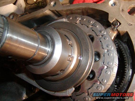 Close-up of engine timing chain and gears, with a metal shaft on the left
