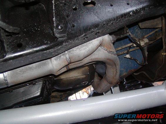 Exhaust manifold and frame of a vehicle, viewed from below. Some rust is visible on the frame