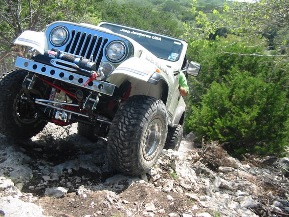 White Jeep CJ-7 with winch and off-road tires climbing rocks