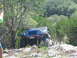 1996 Ford Bronco - A blue Jeep Wrangler navigates a rocky off-road trail surrounded by trees and brush.