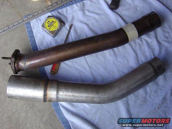 Two exhaust pipes, one copper-colored and one silver, lie on a blue cloth next to a tape measure and screwdriver