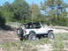 1996 Ford Bronco - A white Jeep Wrangler navigates a , outdoor terrain with sparse vegetation and trees.