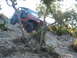 1996 Ford Bronco - An orange Jeep Wrangler navigates a steep, rocky off-road trail with trees and brush.