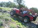 1996 Ford Bronco - A red Jeep Wrangler navigates a steep, rocky incline with sparse vegetation and wildflowers.