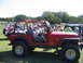 1996 Ford Bronco - Several people gather around off-road vehicles on a sunny day with trees and brush in the background.
