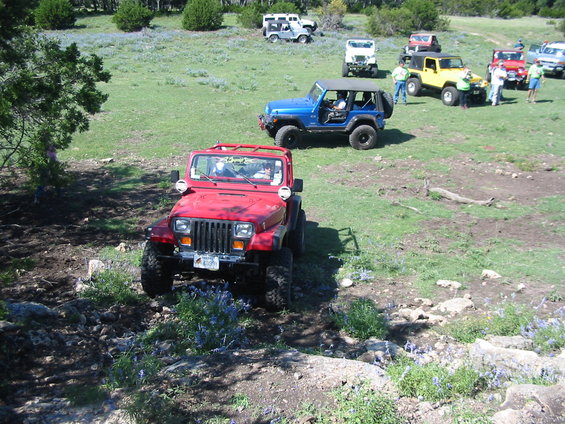 Red Jeep Wrangler with aftermarket bumper and lights, angled front view, on a dirt trail