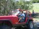 1996 Ford Bronco - A red Jeep Wrangler is driven off-road by a man wearing sunglasses and a blue shirt.
