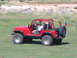 1996 Ford Bronco - A red Jeep Wrangler is parked on a grassy field with a person in the driver's seat.