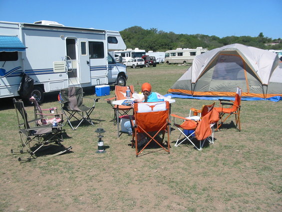 Campsite scene with RVs, tent, and chairs around a table