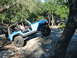 1996 Ford Bronco - A blue Jeep Wrangler navigates a rocky off-road trail with a driver and passenger inside.