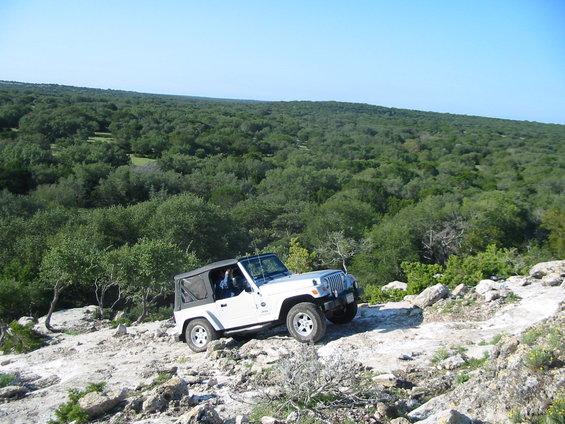 White Jeep Wrangler driving on rocky terrain with a wooded landscape behind