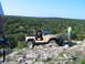 1996 Ford Bronco - A tan Jeep Wrangler navigates a rocky trail under a clear blue sky, with a person observing.