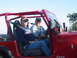 1996 Ford Bronco - Two men are seated inside a red Jeep Wrangler, enjoying a sunny day outdoors.