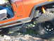 1996 Ford Bronco - Orange Jeep Wrangler navigating rocky terrain, showing its side profile and suspension.