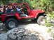 1996 Ford Bronco - This red Jeep Wrangler is navigating a rocky trail with two occupants.