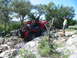 1996 Ford Bronco - A red Jeep Wrangler tackles a challenging off-road course on a sunny day, with a spectator observing the action.