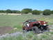 1996 Ford Bronco - A Jeep Wrangler navigates an off-road trail with a driver visible inside. The vehicle is orange and has large tires.