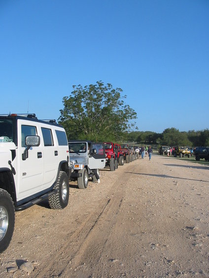 White Hummer H2 in foreground, followed by a line of Jeeps and other SUVs on a dirt road