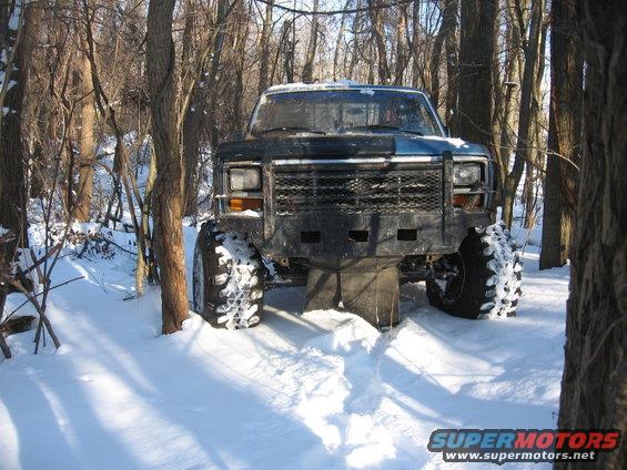 Modified pickup truck with large tires stuck in snow, front view