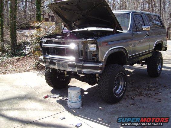 Gray Ford Bronco, hood up, parked on driveway. Lifted suspension and large tires visible
