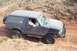 1995 Ford Bronco - A black 1995 Ford Bronco navigates a dusty, off-road trail with a spare tire mounted to the rear.