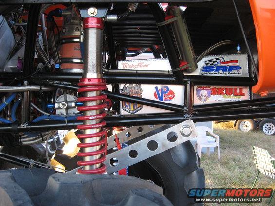 Close-up of custom monster truck suspension with red coilover shock, braided lines, and various racing decals like VP Racing and Skull."