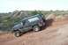 1995 Ford Bronco - A black SUV navigates a steep dirt incline, kicking up dust as it climbs.
