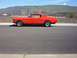 1965 Ford Mustang - A bright red 1965 Ford Mustang coupe is parked on the side of a road with a hilly landscape behind it.