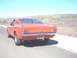 1965 Ford Mustang - Rear view of an orange 1965 Ford Mustang fastback parked on the side of a road with a desert landscape in the background.