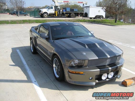 Gray Ford Mustang with black racing stripes parked in a lot. Two round fog lights are mounted on the front bumper