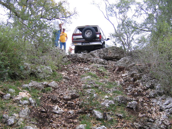 Rear view of a 1996 Ford Bronco climbing a rocky incline with people watching