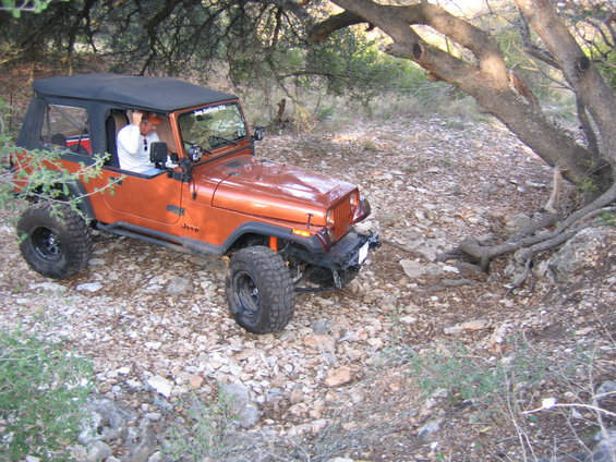 Orange Jeep Wrangler with soft top off-roading on a rocky trail