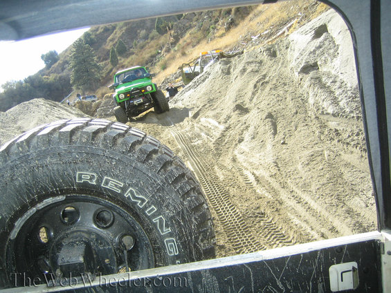 Green off-road vehicle on sandy hill, spare tire in foreground