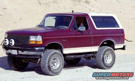 Maroon Ford Bronco with white top, lifted with large tires. Has auxiliary lights on front