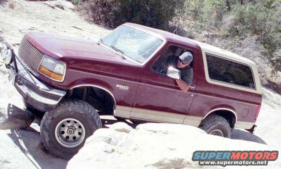Maroon Ford Bronco with tan trim navigating rocky terrain, front-left angle