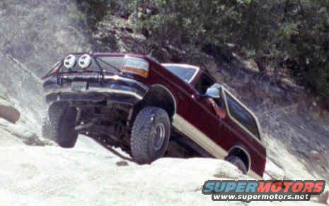 Red 1993 Ford Bronco off-roading on a rocky slope with auxiliary lights